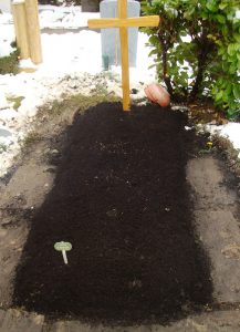 Wenn die Trauerspenden verwelkt oder verblüht sind, wird der Lehm eingeebnet und das Grab mit schwarzer Graberde aufgefüllt.