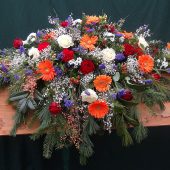 Sarggebinde in Weiß und Blau mit orangen Gerbera und roten Rosen