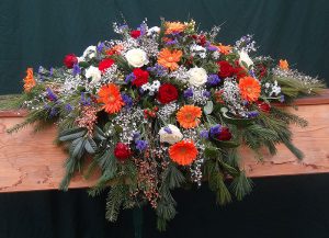 Sarggebinde in Weiß und Blau mit orangen Gerbera und roten Rosen