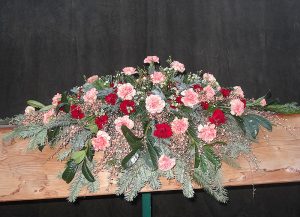 Sarggebinde in Braun und Weiß mit orangen Nelken