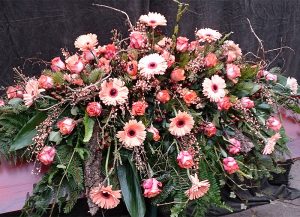 Sarggebinde mit lachsfarbenen Gerbera, Rosen, Wurzeln, Rinde und Efeu