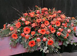 Sarggebinde mit orangen Gerbera, Rosen und Ginster