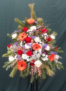 Trauergesteck mit roten und weißen Rosen, orangenen Gerbera und Ginster