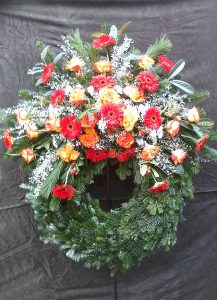 Trauerkranz mit roten Gerbera, orangenen Rosen und weißem Ginster