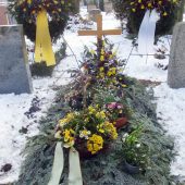 Grab nach der Beisetzung, abgedeckt mit Tannenzweigen und dekoriert mit den Trauergestecken aus der Feierhalle. Die Trauerkränz stehen auf Ständer dahinter.